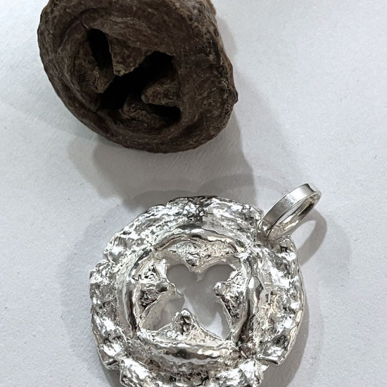 Silver pendant on a white surface with a brown eucaliptus seed beside