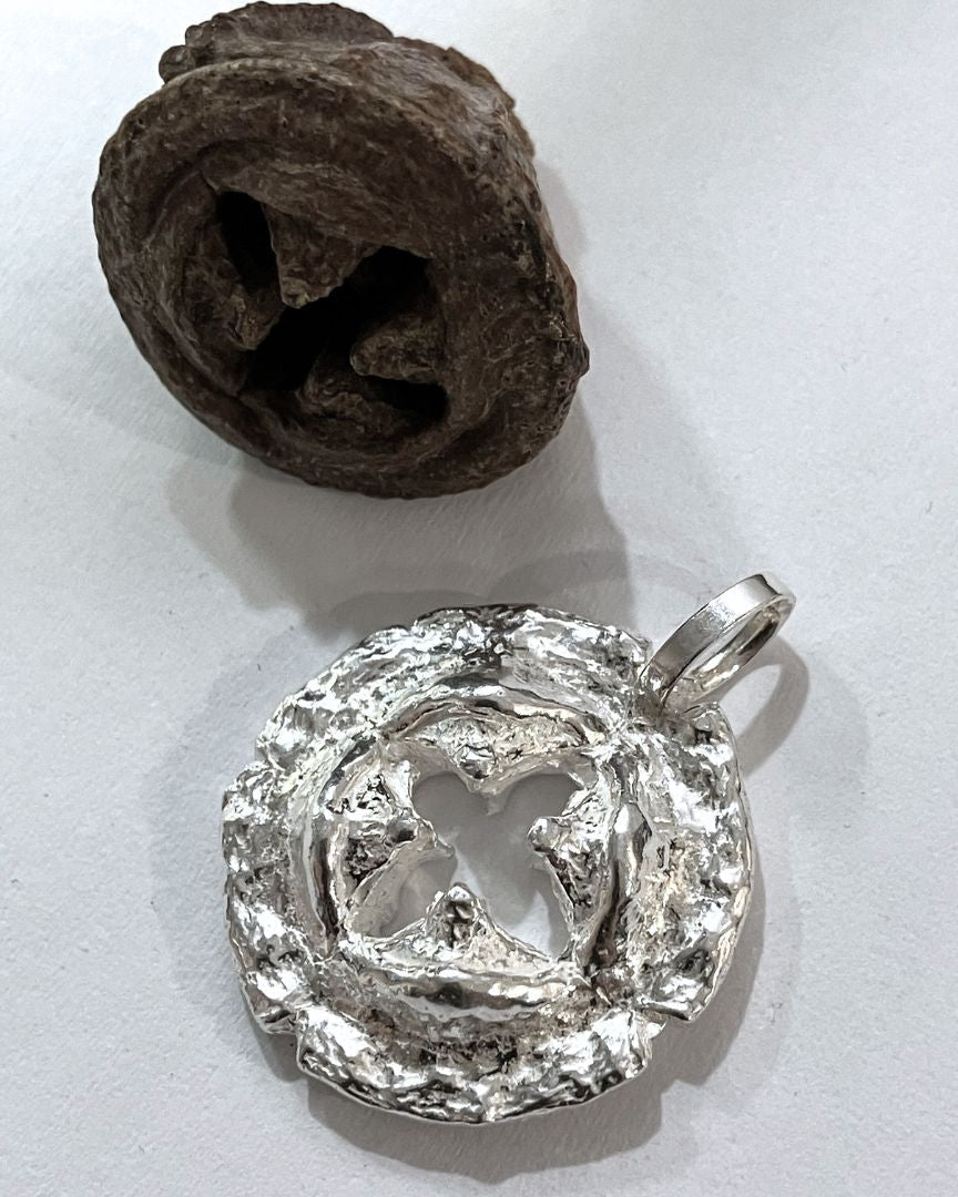 Silver pendant on a white surface with a brown eucaliptus seed beside