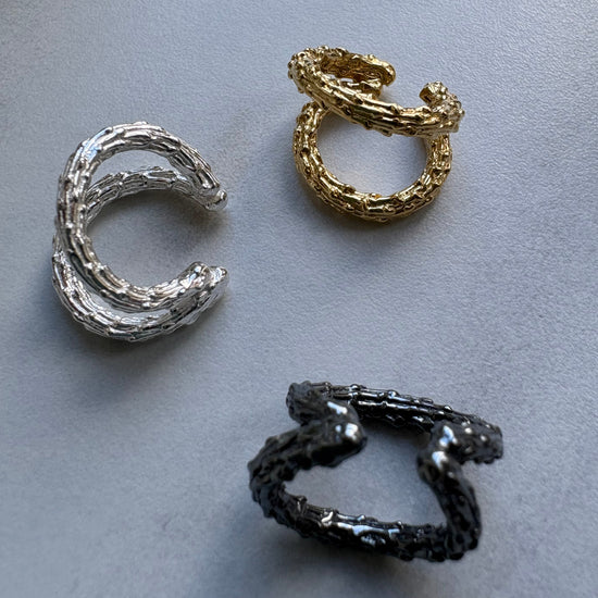 Three pairs of ear cuff earrings in gold, silver, and black on a gray background