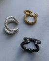 Three pairs of ear cuff earrings in gold, silver, and black on a gray background