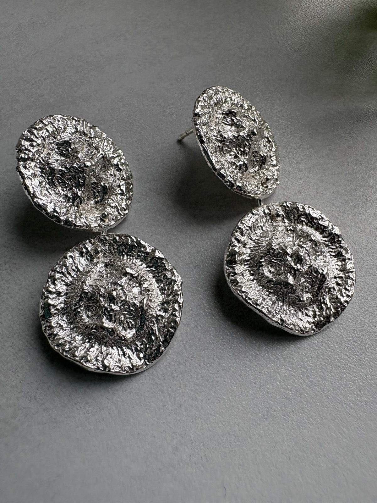 Round and textured pendal silver organic earrings on  a grey surface