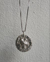 Silver necklace with a round pendant on a gray background
