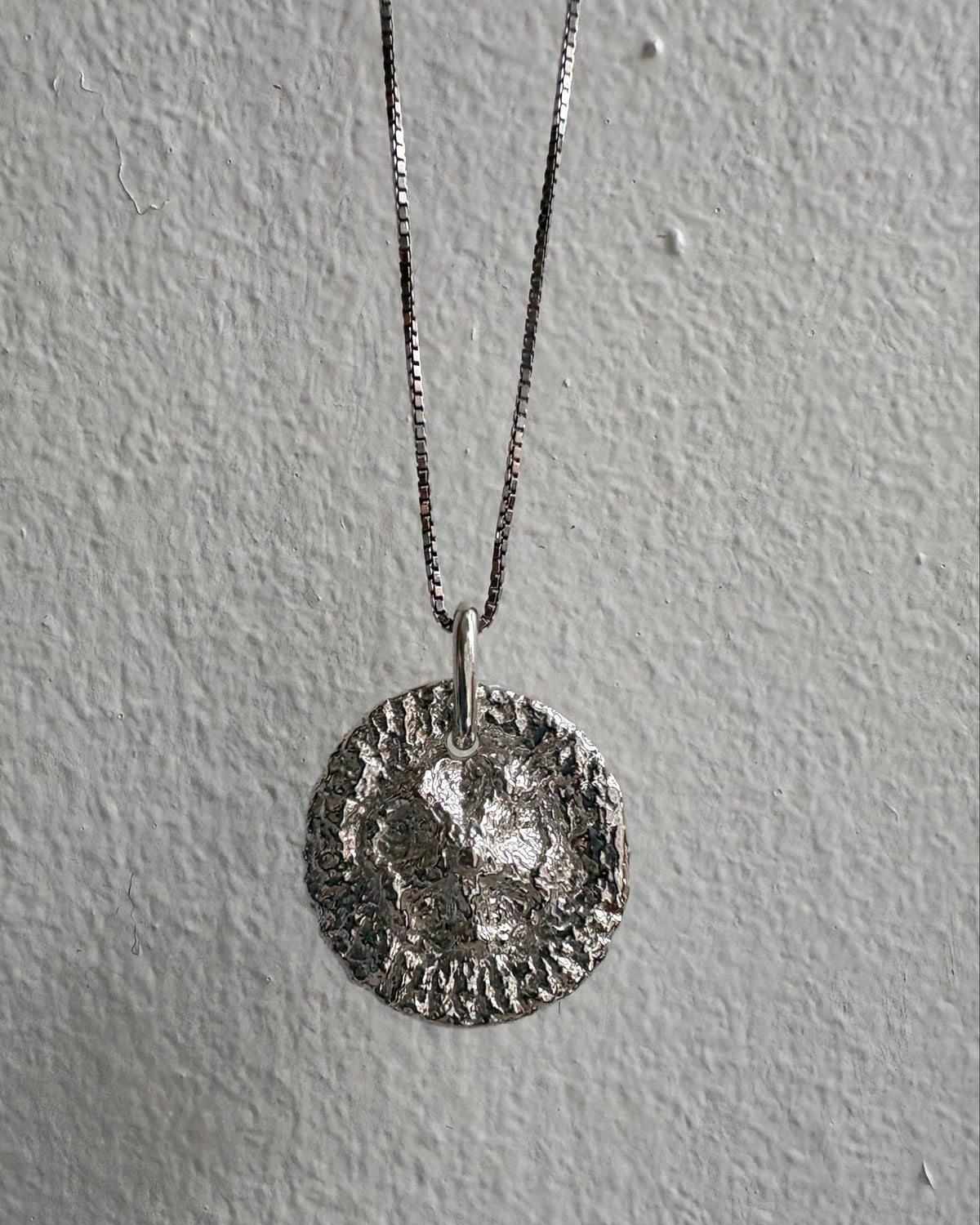 Silver necklace with a round pendant on a gray background