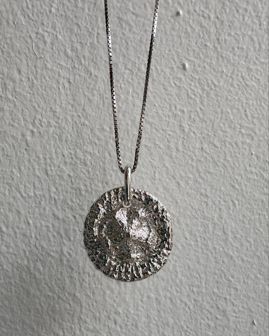 Silver necklace with a round pendant on a gray background