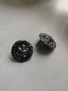 Pair of black rhodium-plated earrings on a light gray surface