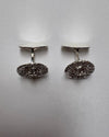 A pair of silver oval cufflinks with textured front, displayed on a neutral light gray background.