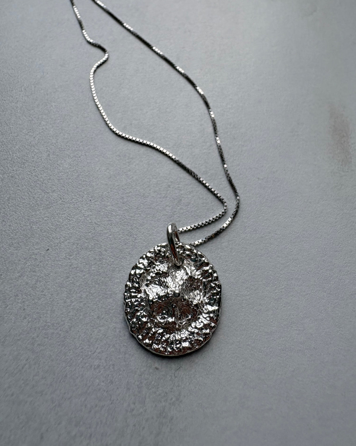 Silver necklace with a textured pendant on a gray surface