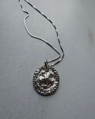 Silver necklace with a textured pendant on a gray surface