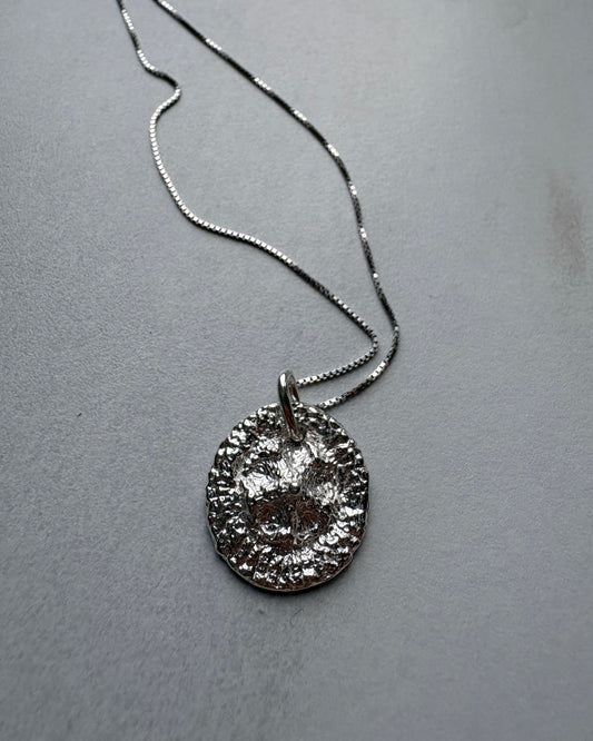 Silver necklace with a textured pendant on a gray surface