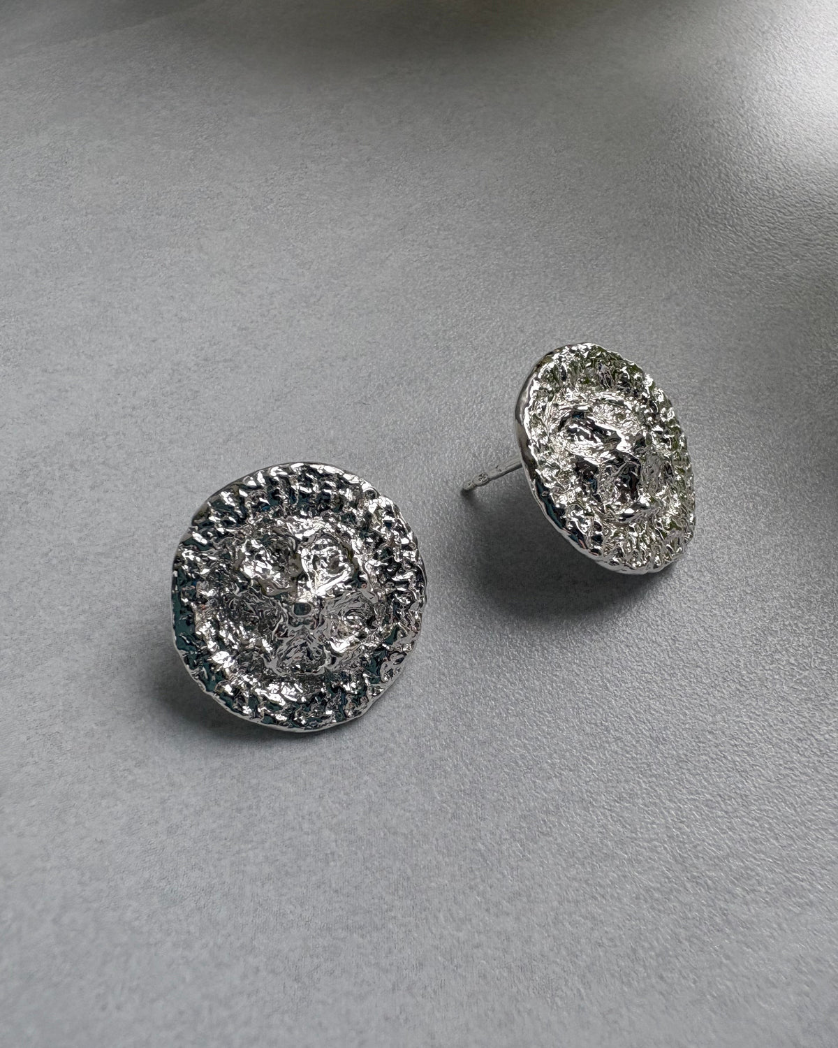Pair of silver stud earrings on a gray surface