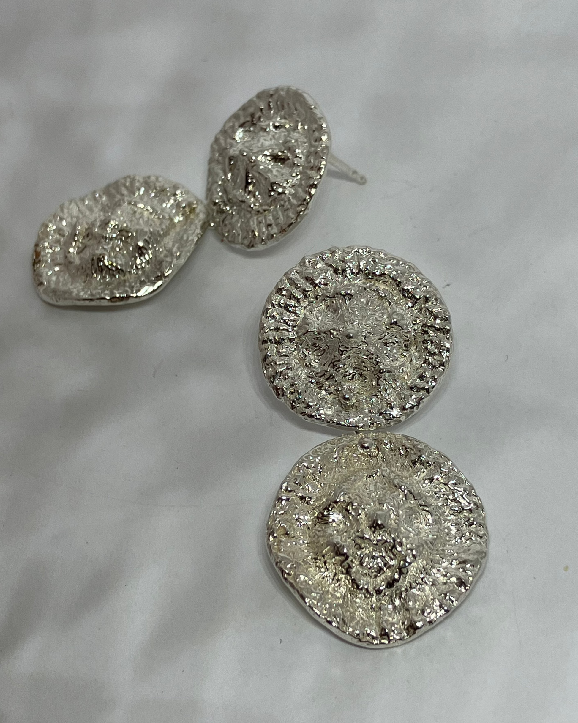 Two round and heavily textured silver earrings on a white  background, and one round stud showing the post back.