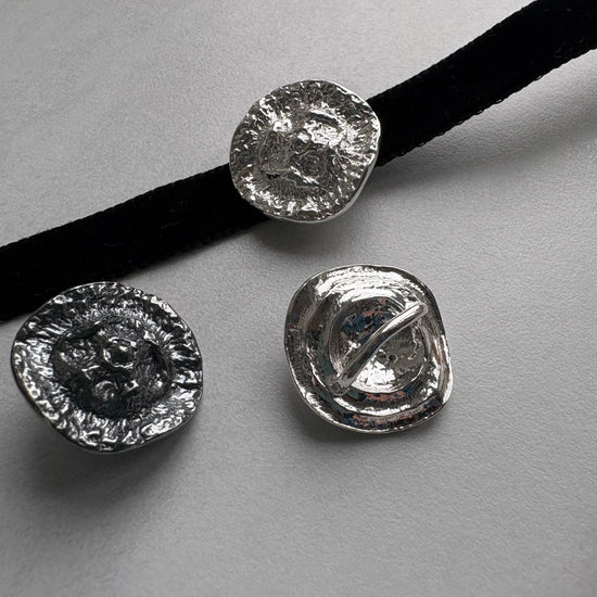 Three silver textured round choker pendants on a gray background