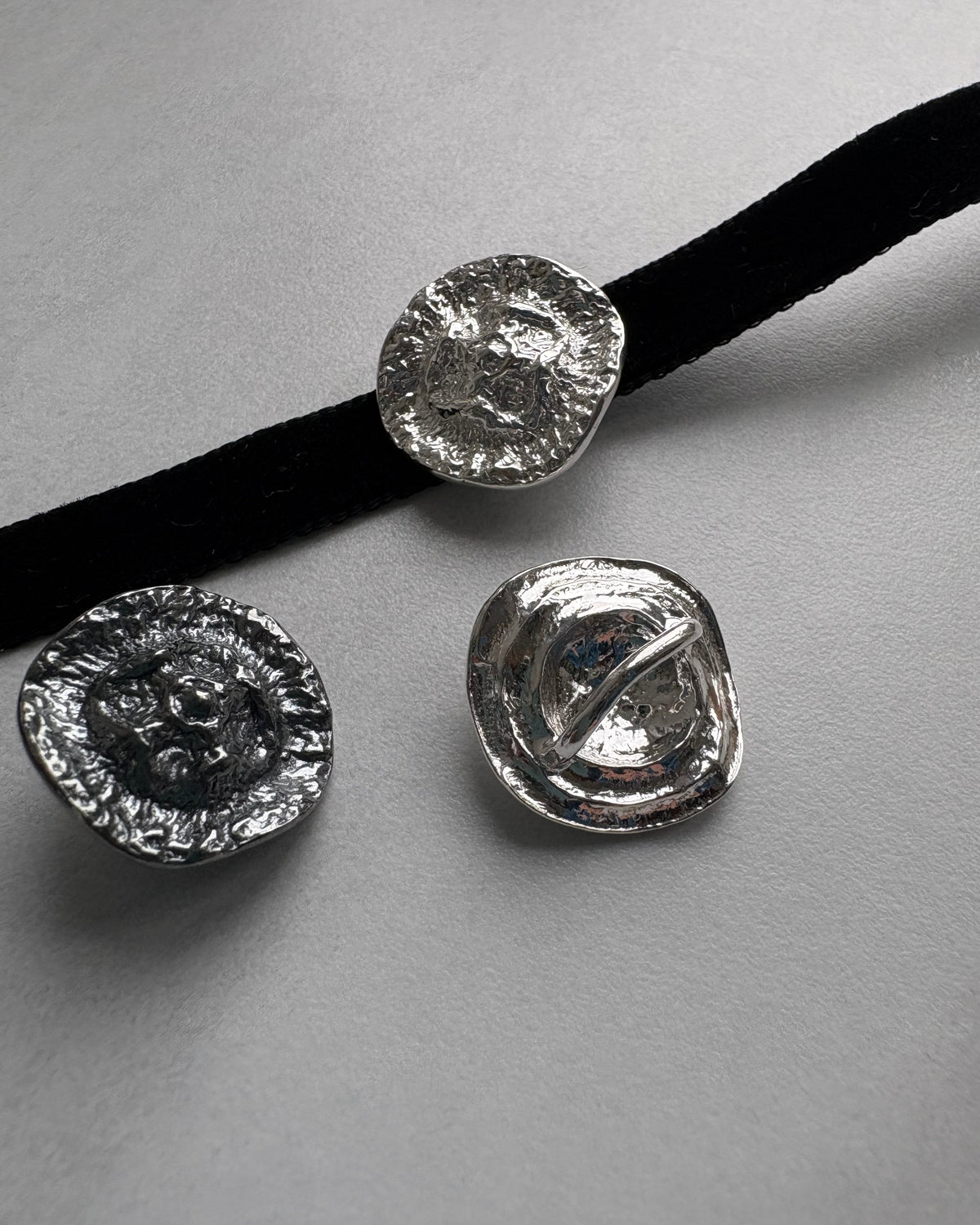 Three silver textured round choker pendants on a gray background