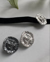 Silver choker pendants on a gray surface with a black ribbon and green leaf.