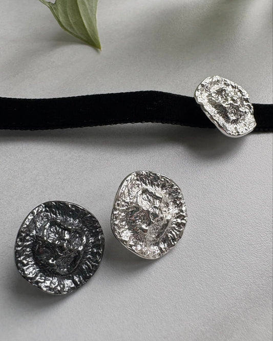 Silver choker pendants on a gray surface with a black ribbon and green leaf.