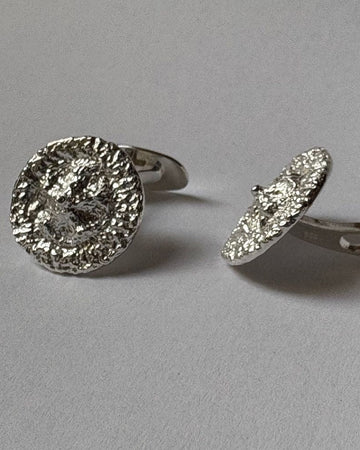 A pair of silver-toned cufflinks with textured, hammered circular faces, shown on a neutral gray background.