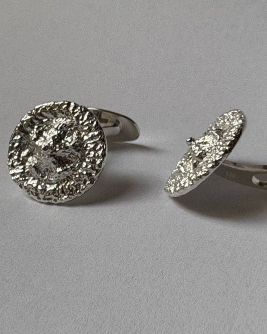A pair of silver-toned cufflinks with textured, hammered circular faces, shown on a neutral gray background.