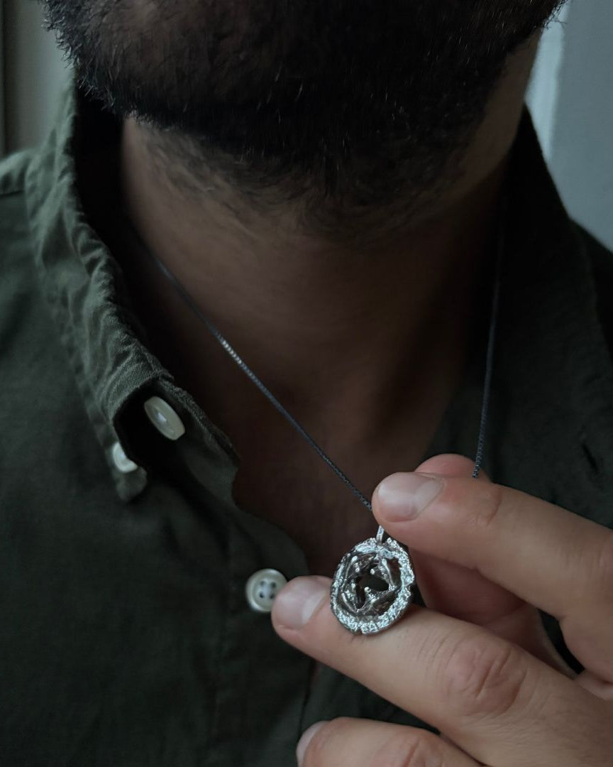 Person holding a necklace with a diamond pendant close to their face.