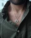 Man wearing a green shirt with a necklace featuring a circular pendant.