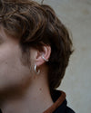close up of model wearing a silver textured hoop and silver earcuff in the same style on a beige background