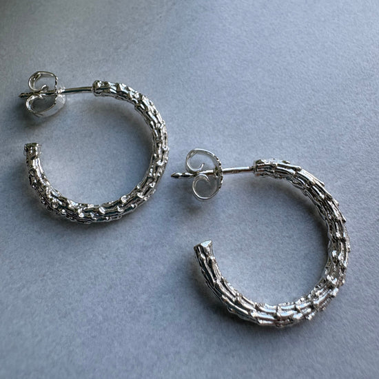 Pair of textured silver hoop earrings on a gray background