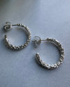 Pair of textured silver hoop earrings on a gray background
