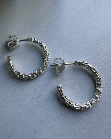 Pair of textured silver hoop earrings on a gray background