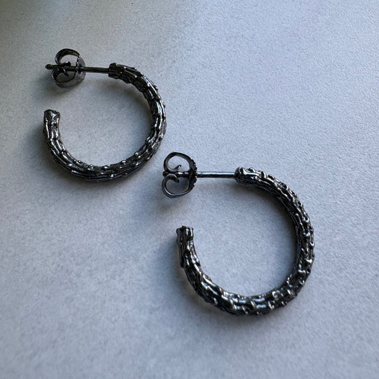 Pair of oxidised silver hoop earrings on a light gray surface