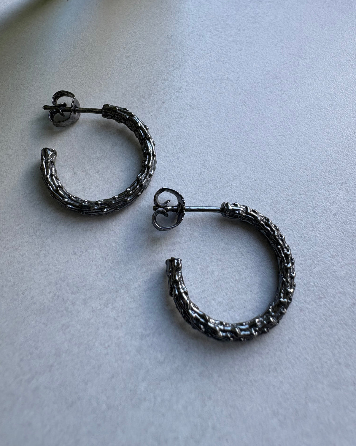 Pair of oxidised silver hoop earrings on a light gray surface