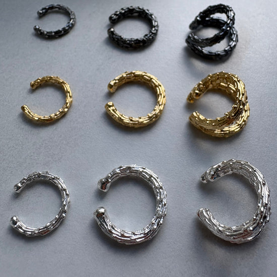 Set of gold, silver, and black hoop earrcuffs on a gray background
