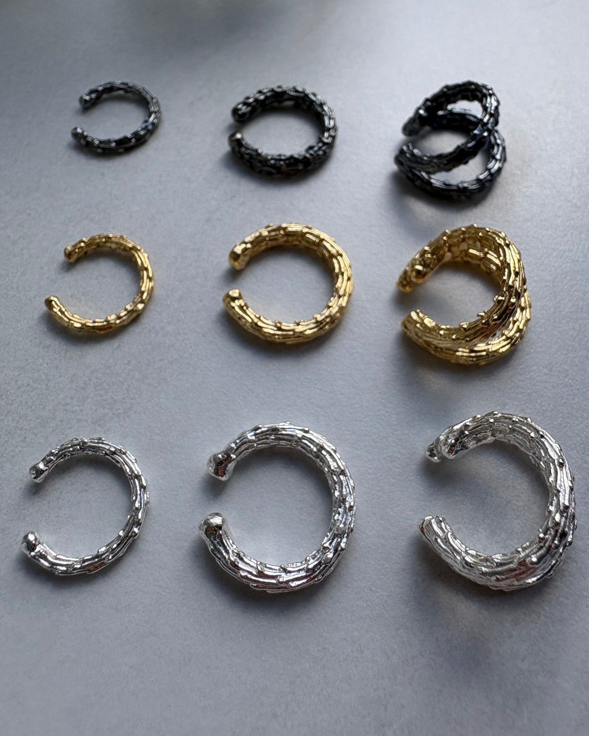 Set of gold, silver, and black hoop earrcuffs on a gray background