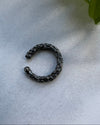 Black metal earcuff on a light gray surface with a green leaf in the corner