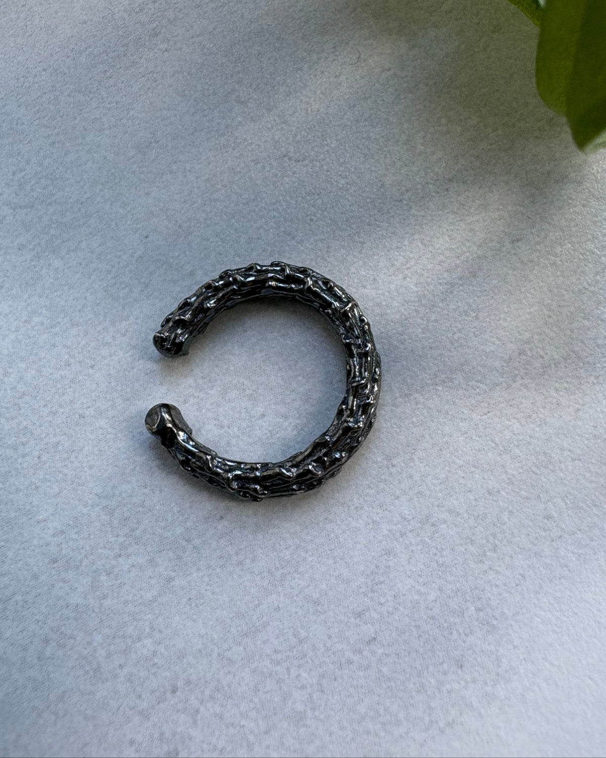Black metal earcuff on a light gray surface with a green leaf in the corner