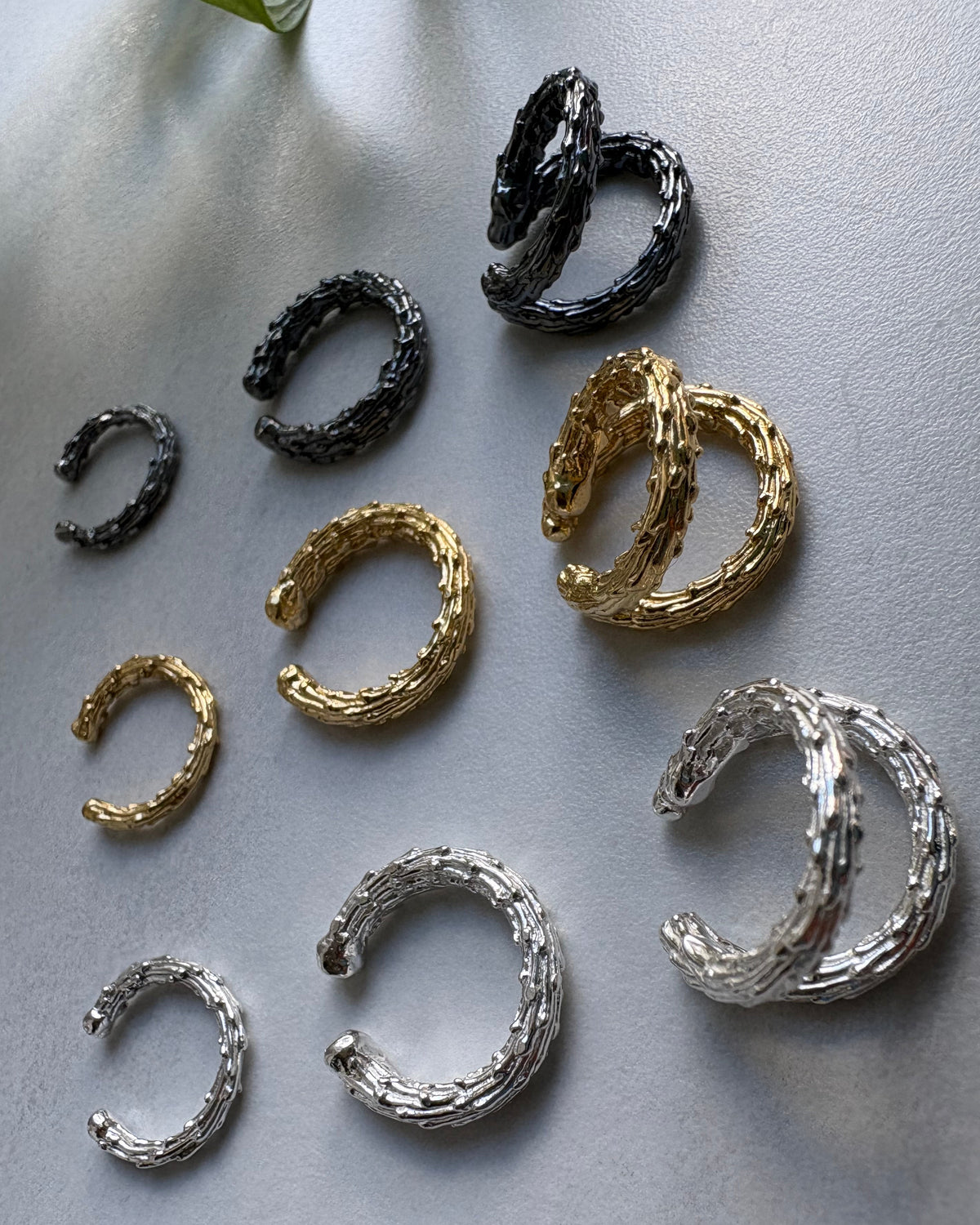 Set of gold, silver, and black hoop earcuffs on a gray surface