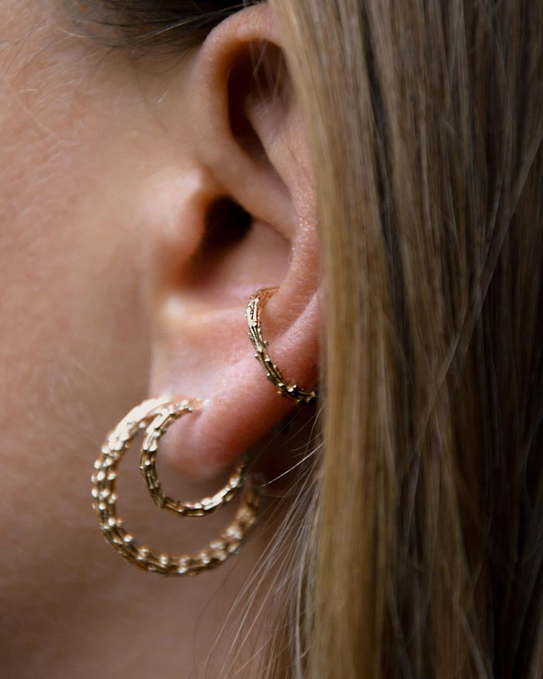 Close-up of a person wearing gold hoop earrings with a blurred background