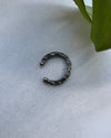 Oxidised silver earcuff  with a textured design on a light gray surface with a green leaf.