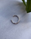 Silver hoop ear cuff on a light gray surface with a green leaf in the corner.