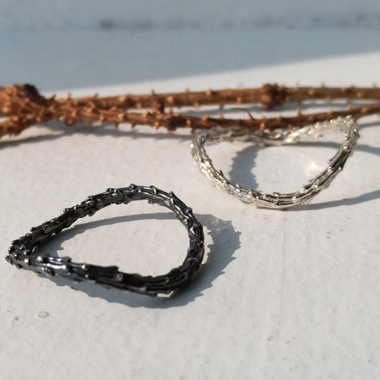 two organic silver rings one with black oxidation and branches of pine tree in the background
