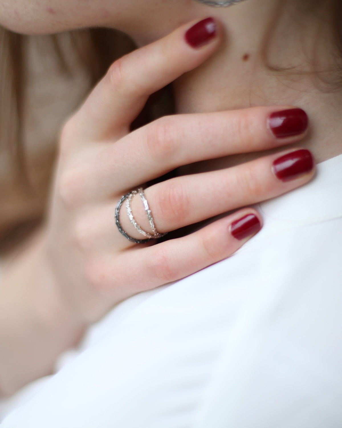 Close-up of a hand with red nail polish wearing multiple silver rings on a blurred background