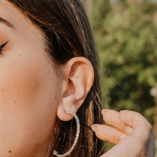 Woman with closed eyes, wearing hoop earrings and a striped garment against a blue sky.