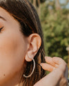 Woman with closed eyes, wearing hoop earrings and a striped garment against a blue sky.