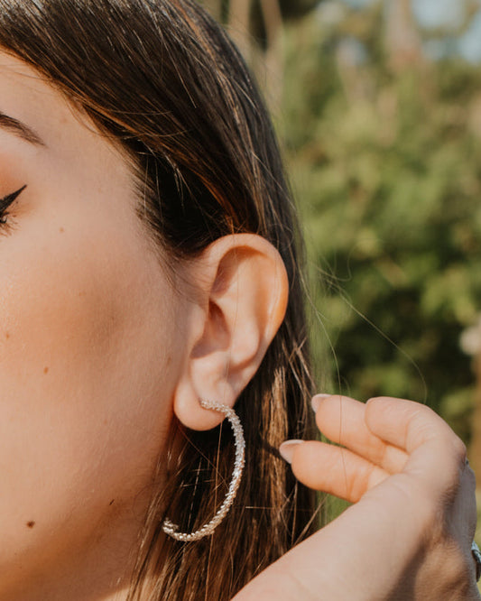 Woman with closed eyes, wearing hoop earrings and a striped garment against a blue sky.