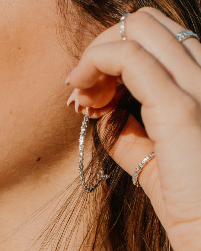 Woman adjusting her earrings with a blurred natural background