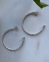 Silver hoop earrings on a light gray surface with a green leaf in the corner.