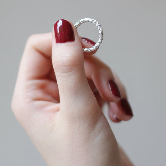 hand holding an organi silver ring on a grey background