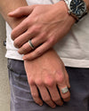 Close-up of two hands with rings, one wearing a watch, against a neutral background.