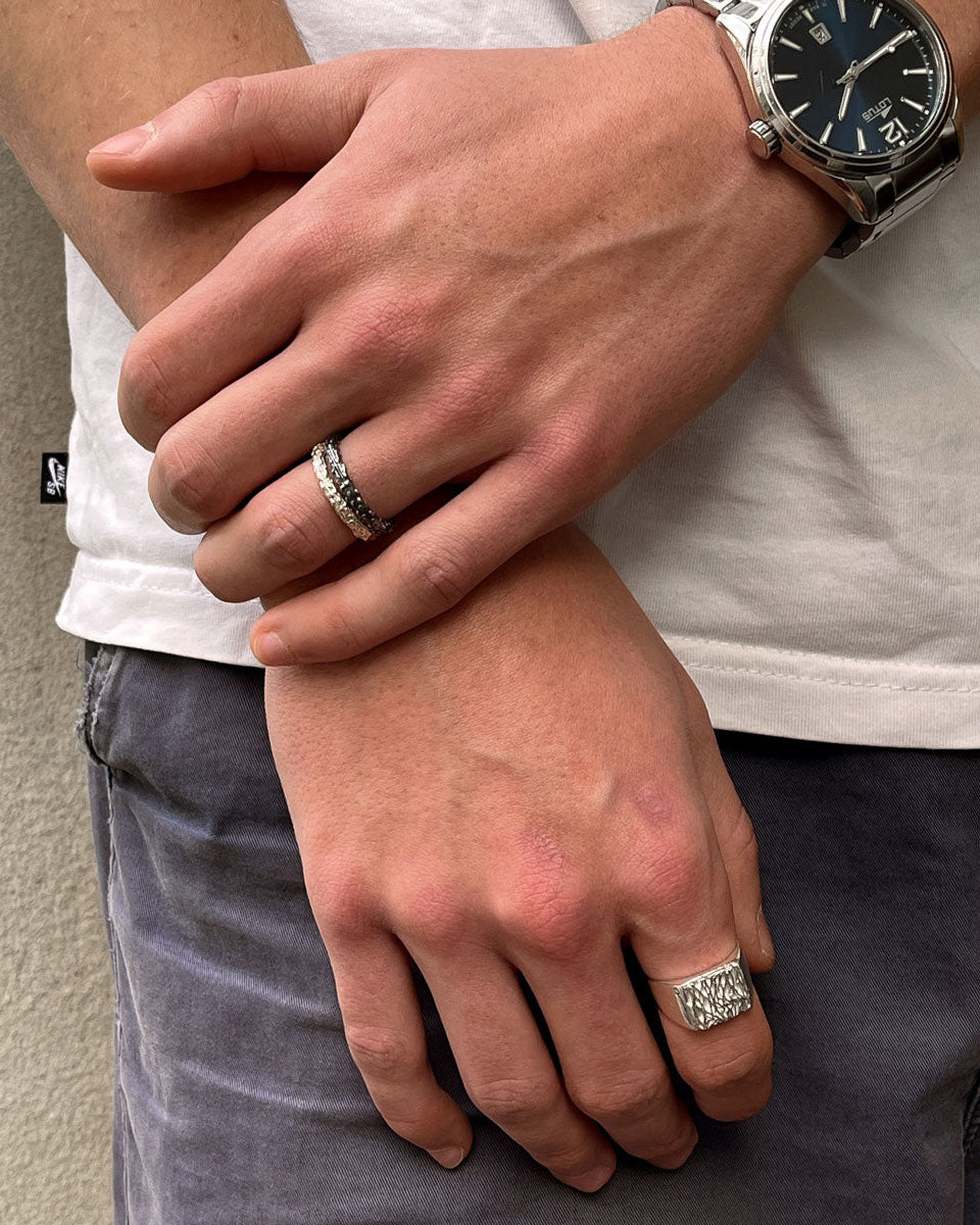 Close-up of two hands with rings, one wearing a watch, against a neutral background.