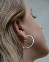 Close-up of a person wearing organic silver hoops and earcuff with a neutral background