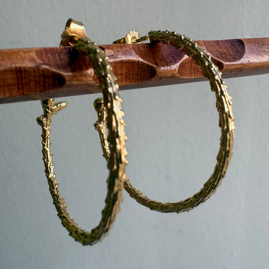 wooden stick holding two organic hoops earrings gold color