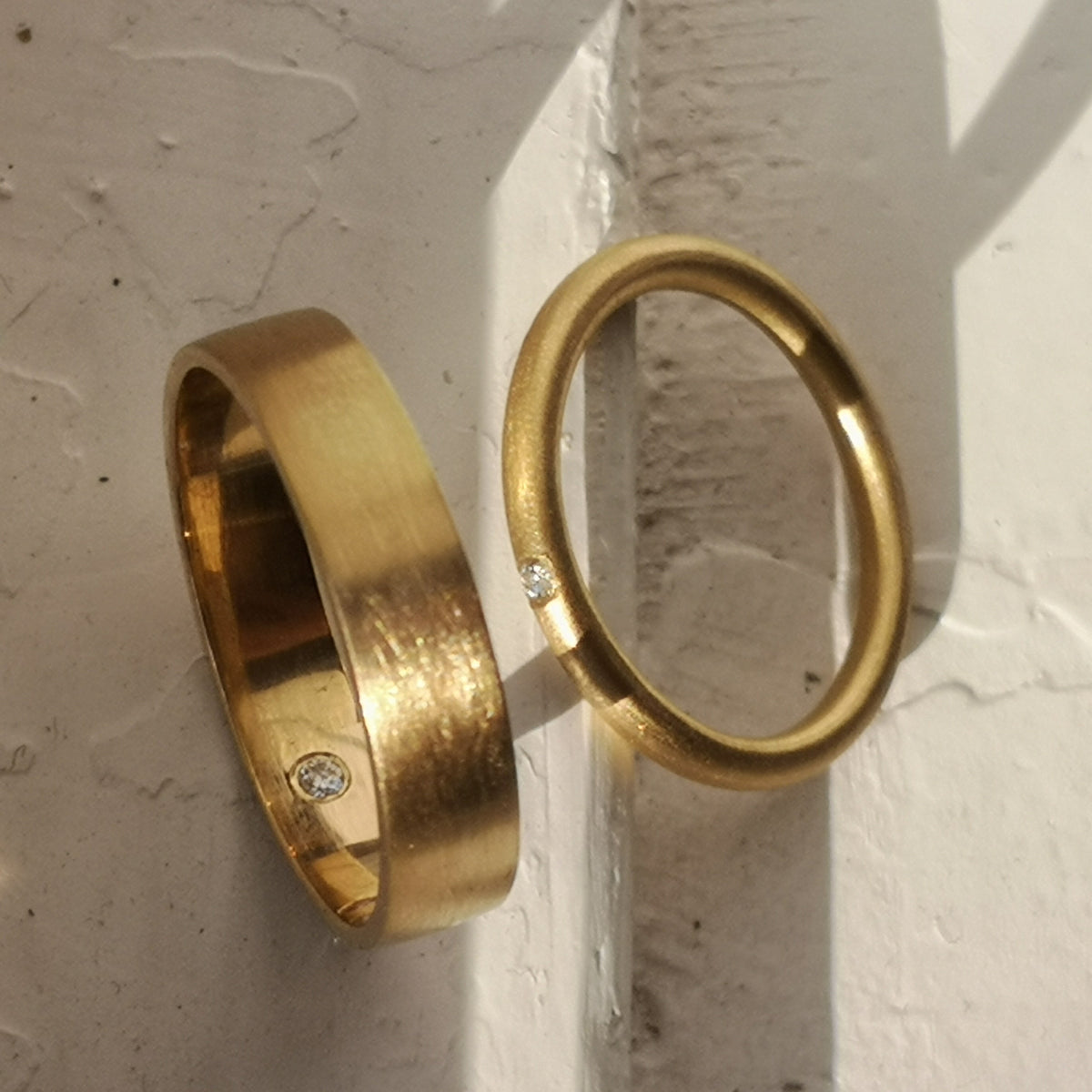 Two gold rings with small diamonds on a textured white surface